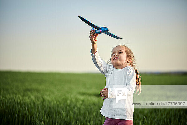 Verspieltes Mädchen fliegt Spielzeugflugzeug auf dem Feld bei Sonnenuntergang