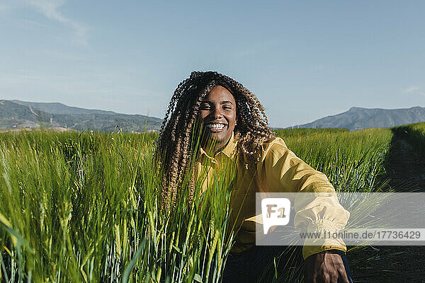 Glückliche Frau mit lockigem Haar  die an einem sonnigen Tag im Gras sitzt