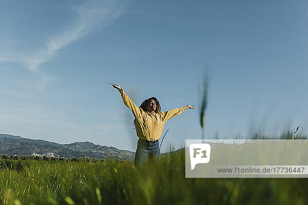 Young woman standing with arms outstretched under blue sky