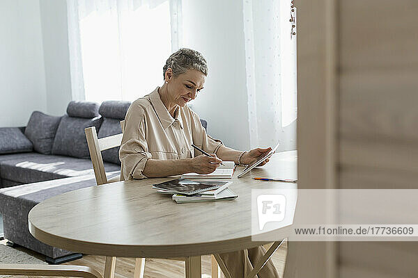 Frau nutzt digitales Tablet und macht sich zu Hause am Tisch Notizen
