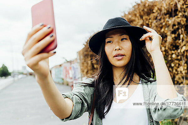 Beautiful young woman wearing hat taking selfie through smart phone