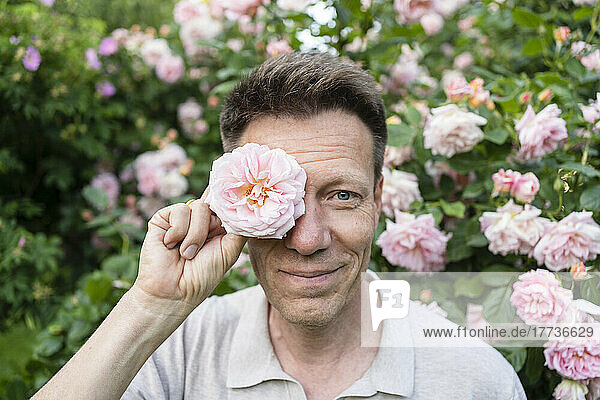 Smiling man holding rose in front of eye at garden