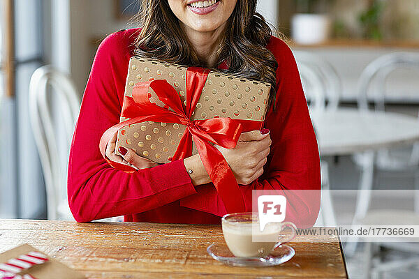 Happy woman with Christmas present sitting at table in cafe