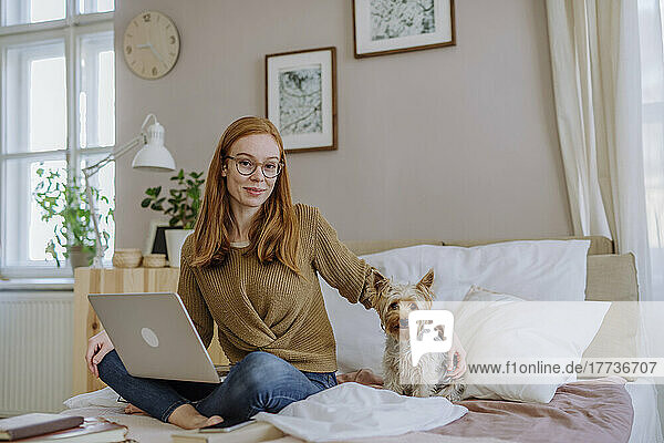 Smiling woman with Yorkshire Terrier sitting on bed at home