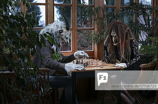 Man and woman in spooky costumes playing chess sitting at table