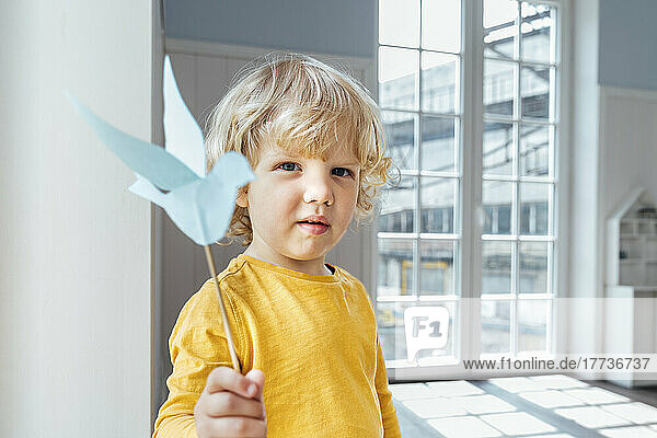 Cute boy with origami bird standing at home