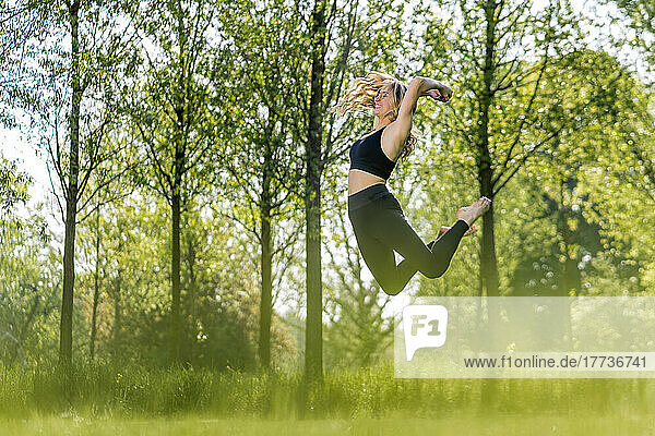 Happy woman jumping at park on sunny day