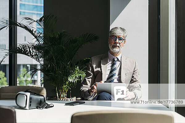 Businessman with tablet PC sitting at desk in office