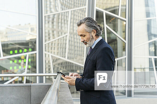 Mature businessman using mobile phone standing by railing