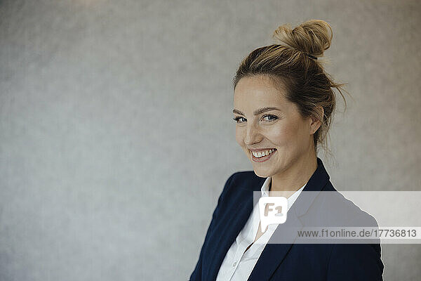 Happy businesswoman with blond hair bun in front of gray wall