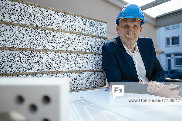Businessman wearing hardhat by blueprint at construction site