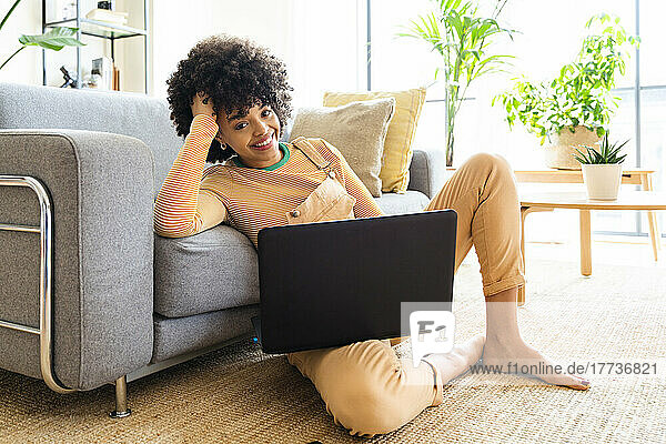Happy woman with laptop leaning on sofa at home