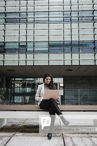 Dedicated young businesswoman sitting on bench using laptop