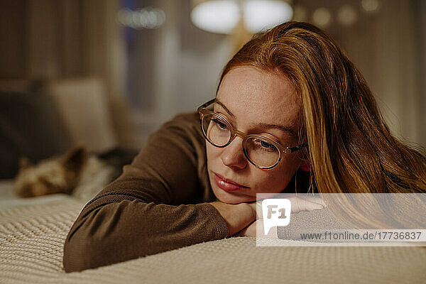 Sad redhead woman lying on bed at home