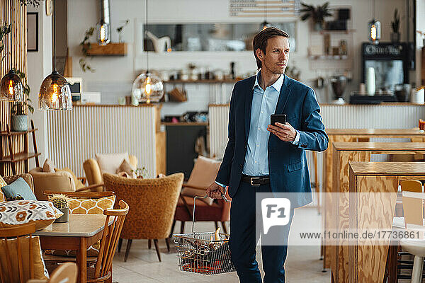 Mature businessman with basket of vegetables and smart phone at cafe