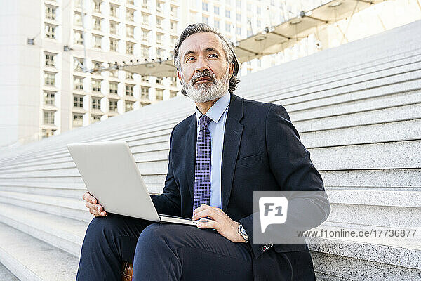 Mature businessman with laptop sitting on staircase