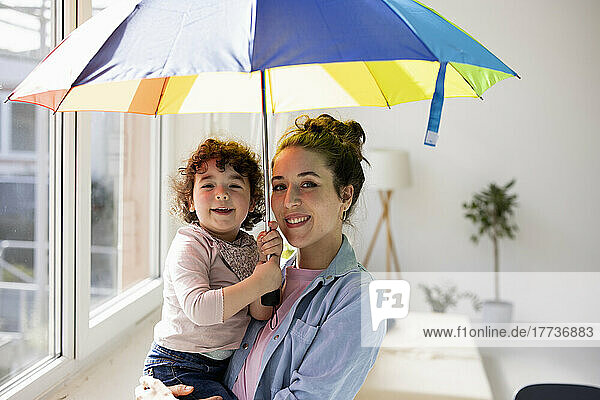 Mother and daughter standing at home holding umbrella