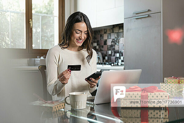 Happy woman with credit card doing online shopping through smart phone at home