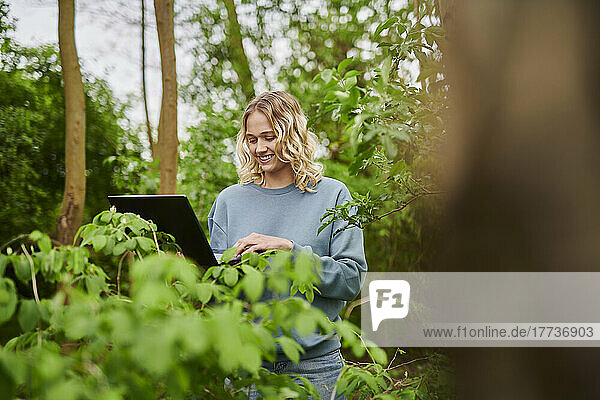 Smiling freelancer using laptop by plants in forest