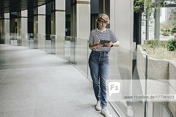 Woman using tablet PC leaning on glass railing at arcade