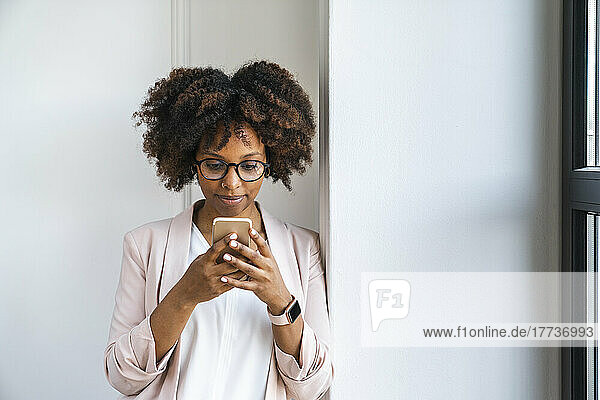 Woman using smart phone by white wall at workplace