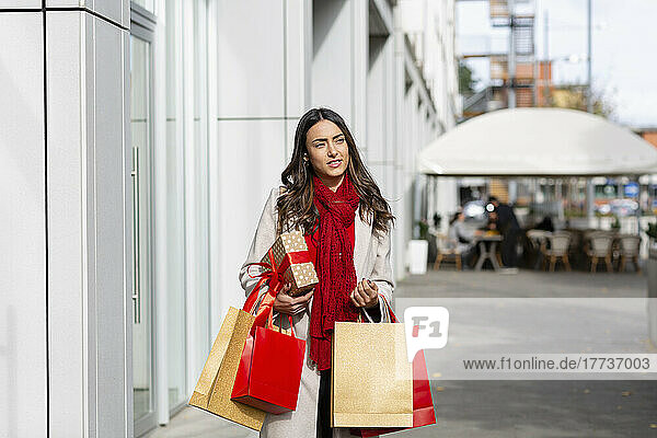 Young woman with Christmas present and shopping bags on sunny day