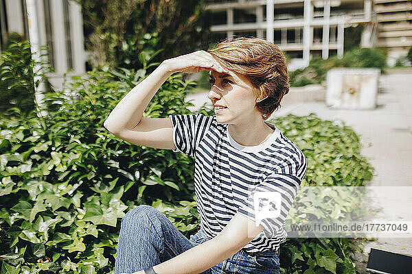 Woman shielding eyes sitting by plants