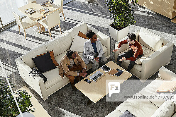 Young businessmen and businesswoman discussing strategy sitting on sofa in modern office