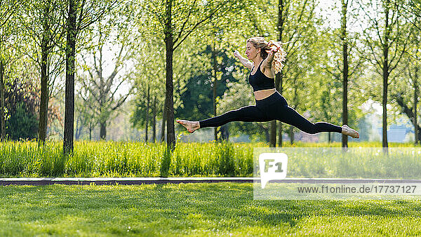 Young woman with arms outstretched jumping on meadow at park