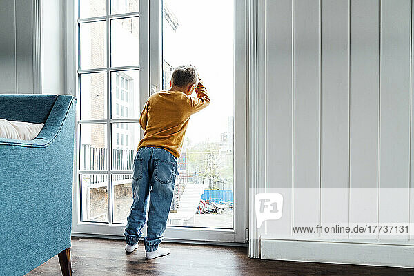 Boy leaning on glass window at home