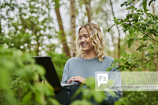 Happy freelancer working amidst trees in forest