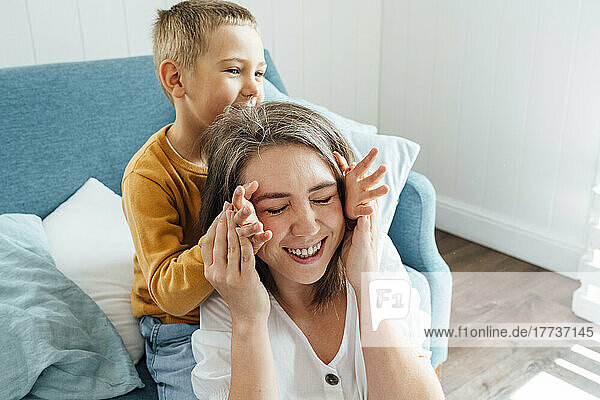 Glückliche Mutter spielt mit ihrem Sohn  der zu Hause auf dem Sofa im Wohnzimmer sitzt