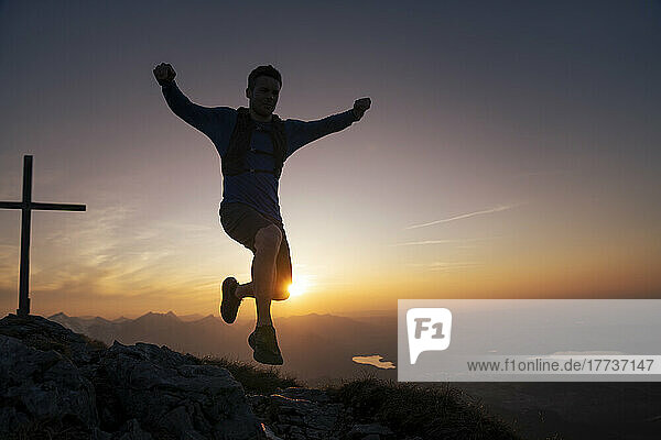 Wanderer springt bei Sonnenuntergang auf den Berggipfel