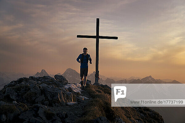Hiker running on top of Sauling mountain peak with summit cross