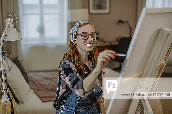 Happy woman wearing bandana painting on artist's canvas at home