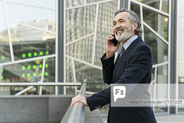 Happy businessman talking on smart phone standing by railing