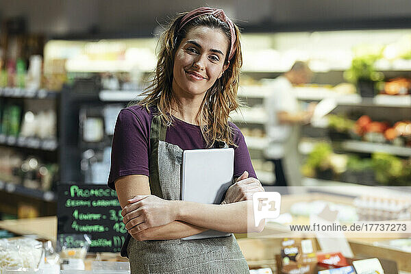 Smiling store owner standing with tablet PC at organic market