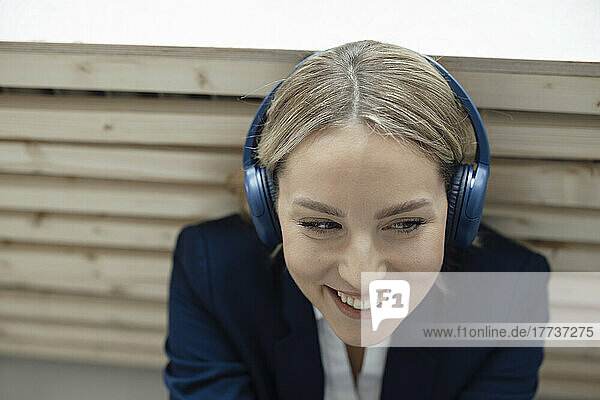 Smiling businesswoman enjoying music listening through wireless headphones leaning on radiator in office