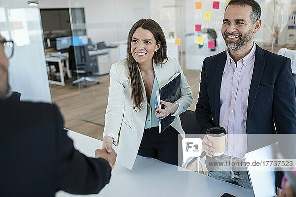 Smiling businesswoman standing colleague greeting businessman in office