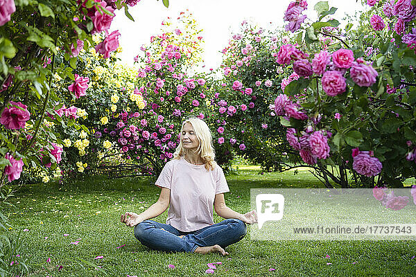 Woman with eyes closed meditating amidst rose garden