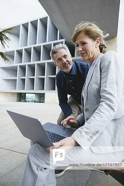 Businesswoman with laptop sitting by businessman