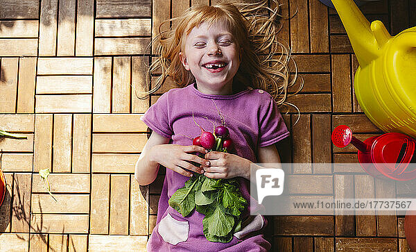 Happy girl lying with radish on balcony floor