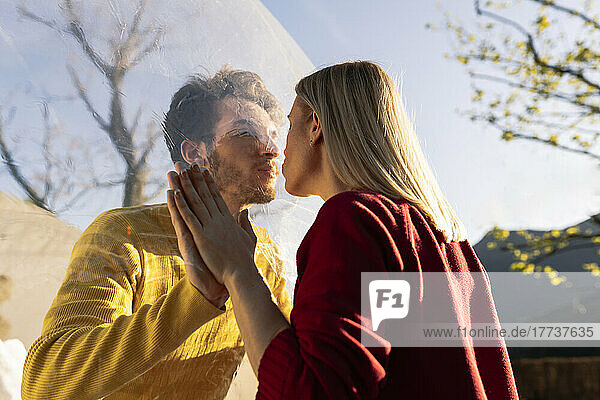 Man kissing girlfriend through transparent dome hotel on sunny day