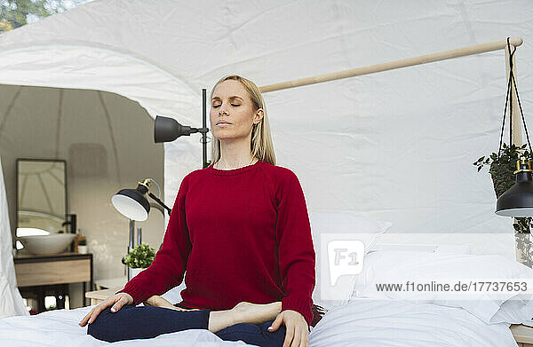 Woman doing meditation sitting on bed in hotel room