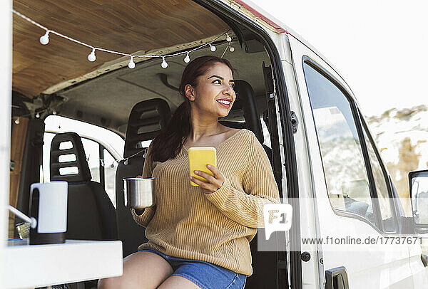 Smiling woman holding smart phone sitting in motor home