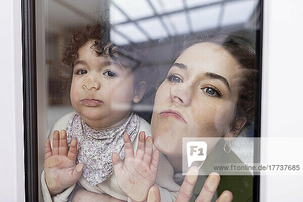 Mutter und Tochter schauen durchs Fenster und drücken ihre Gesichter auf die Glasscheibe