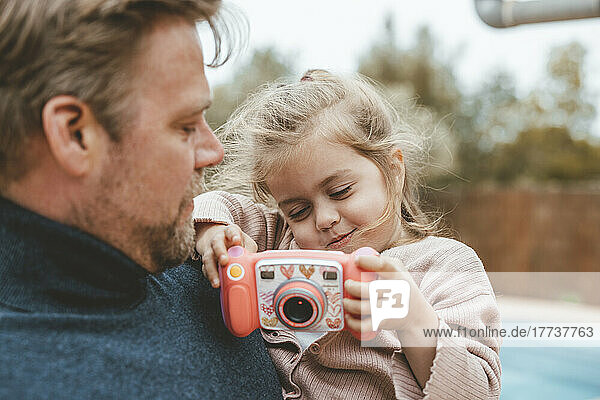 Father carrying daughter playing with toy camera