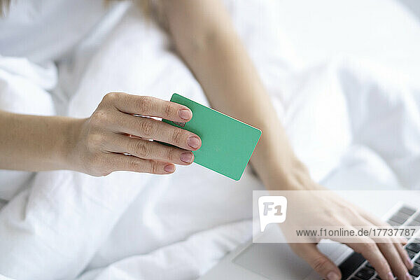 Frau hält Kreditkarte und benutzt Laptop auf dem Bett