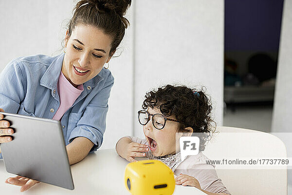 Working mother sitting at table daughter playing with AI toy robot
