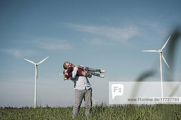 Happy man carrying daughter standing in field on sunny day